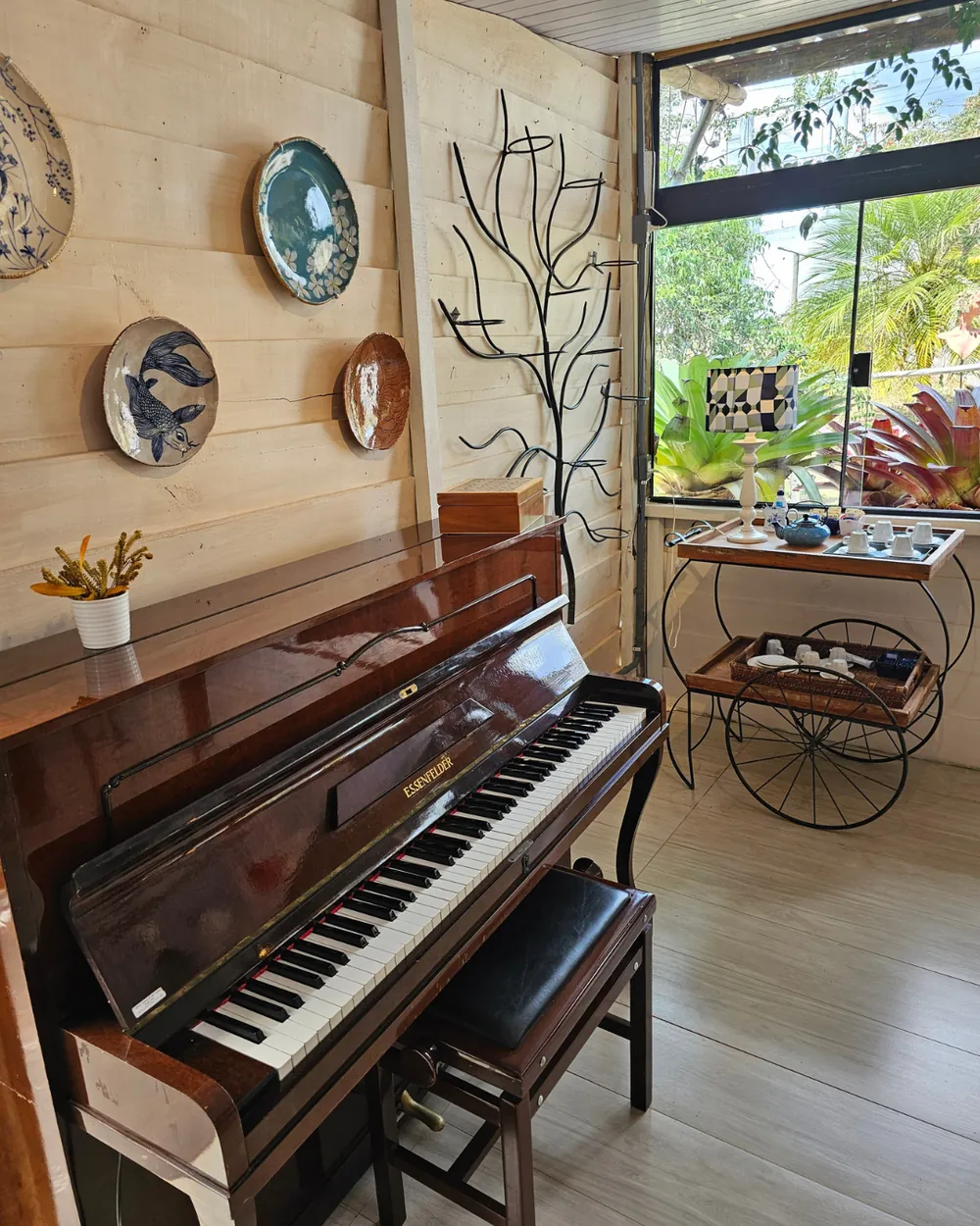 O piano do salão, com pratos de cerâmica pintados na parede e a janela aberta para o jardim