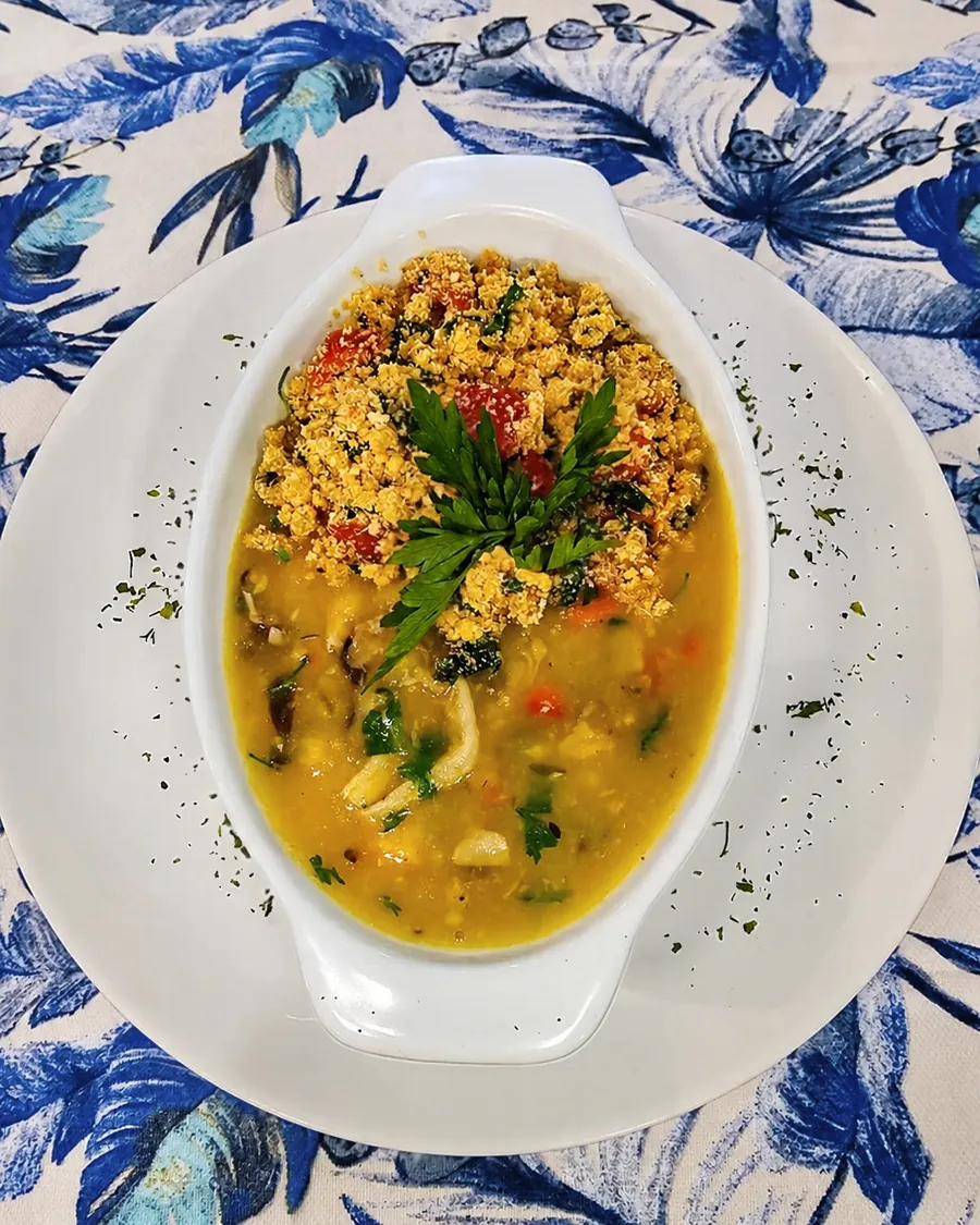 Caldeirada da Serra: moqueca de cogumelos e mandioca em travessa branca, coberta de farofa colorida