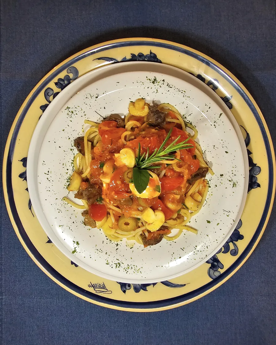 Sertão: espaguete com cubos de filé mignon, tomate-cereja e azeitonas em prato de borda azul