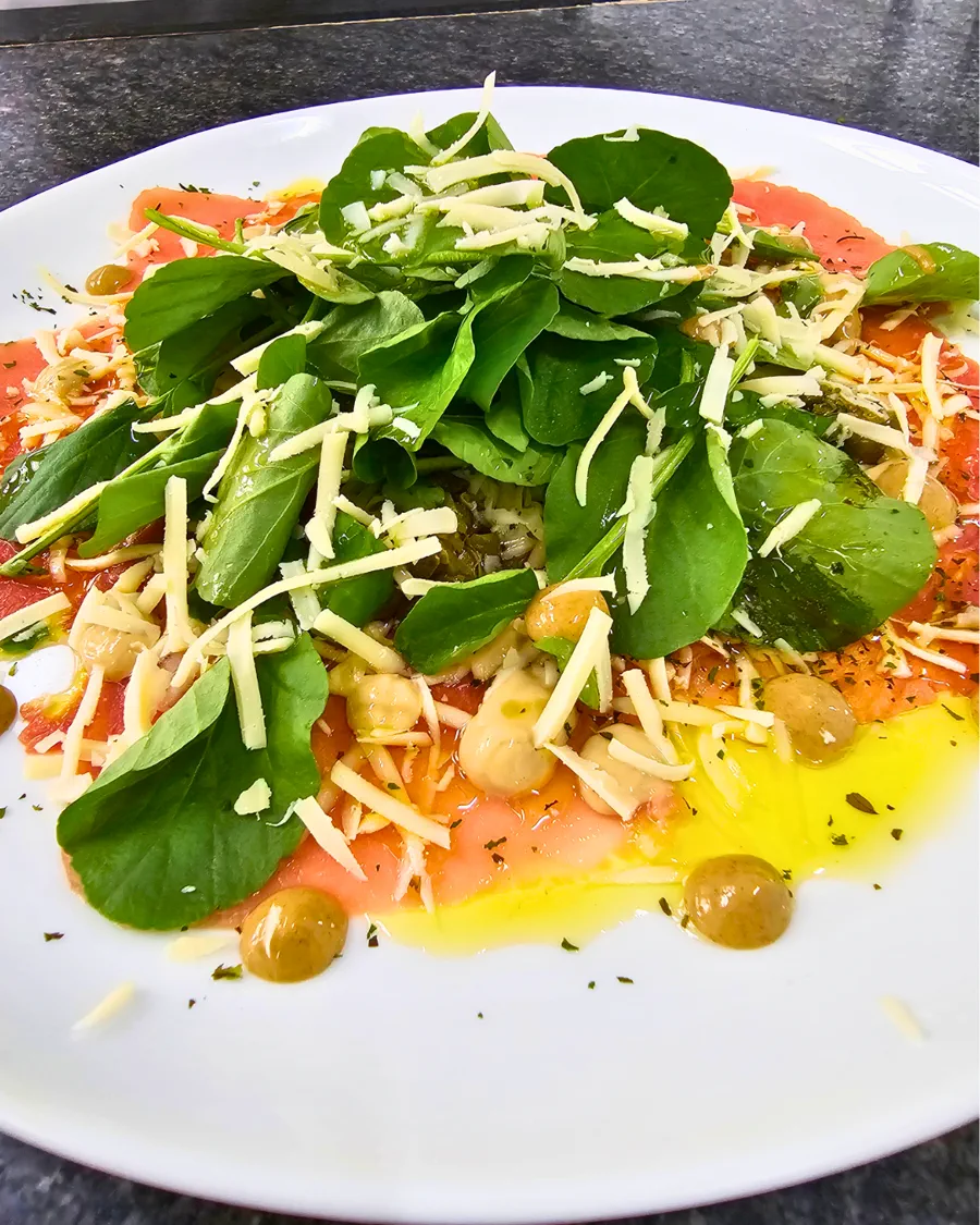 Vermelho e Verde: carpaccio coberto de folhas de rúcula e lascas de parmesão em prato branco