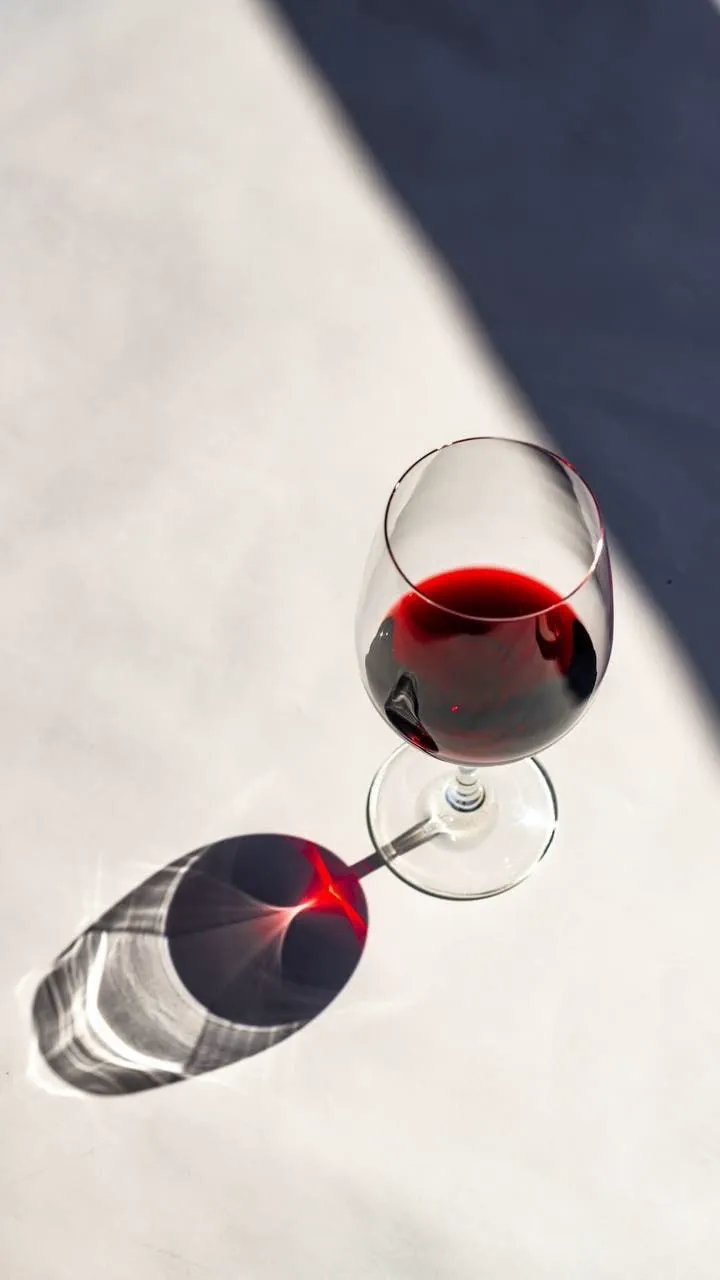 Taça de vinho tinto sobre a mesa branca, com a sombra do sol