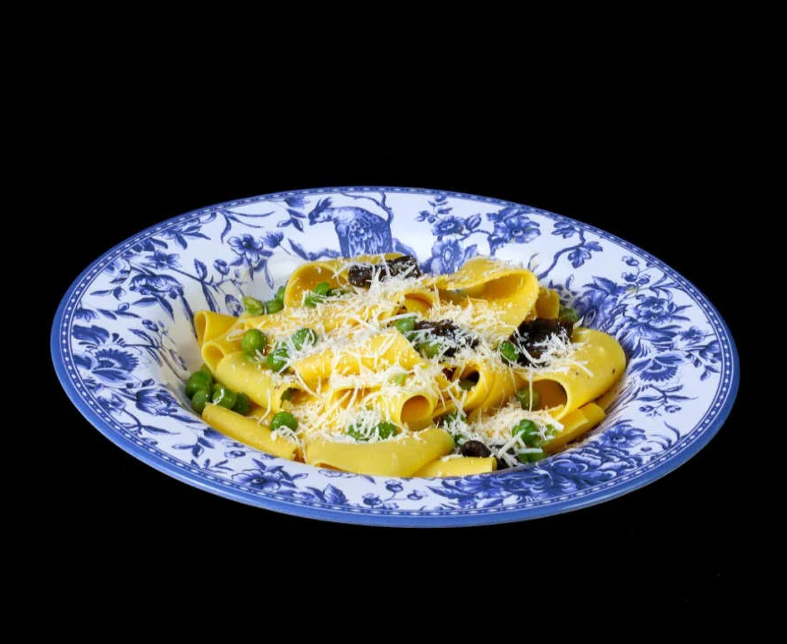 Enlace: pappardelle amarelo com ervilhas e queijo ralado em prato de louça azul e branca